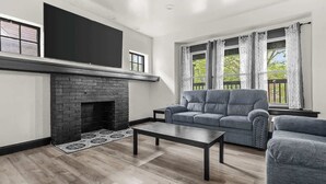 Ein modernes Wohnzimmer mit Kamin, einer Couch, einem Couchtisch und einem großen Fenster mit Vorhängen.