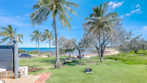 A grassy area with palm trees, a beach, and a clear blue sky. - Shoreline Apartments - Unit 4a (Bargara)