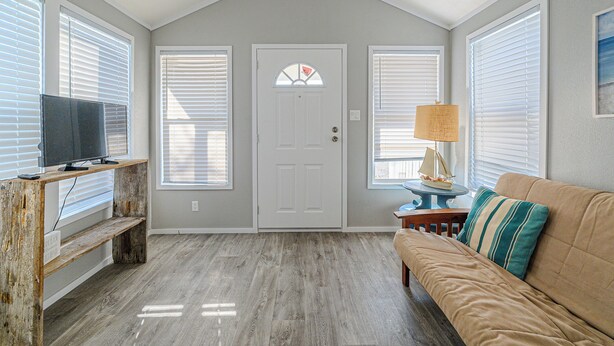 Une pièce avec un plancher en bois, un canapé beige, un téléviseur posé sur un meuble en bois et une porte avec une fenêtre.
