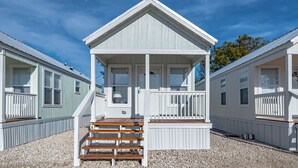 Un chalet situé en bord de mer, doté d’un porche couvert, d’un escalier en bois et d’une allée en gravier.
