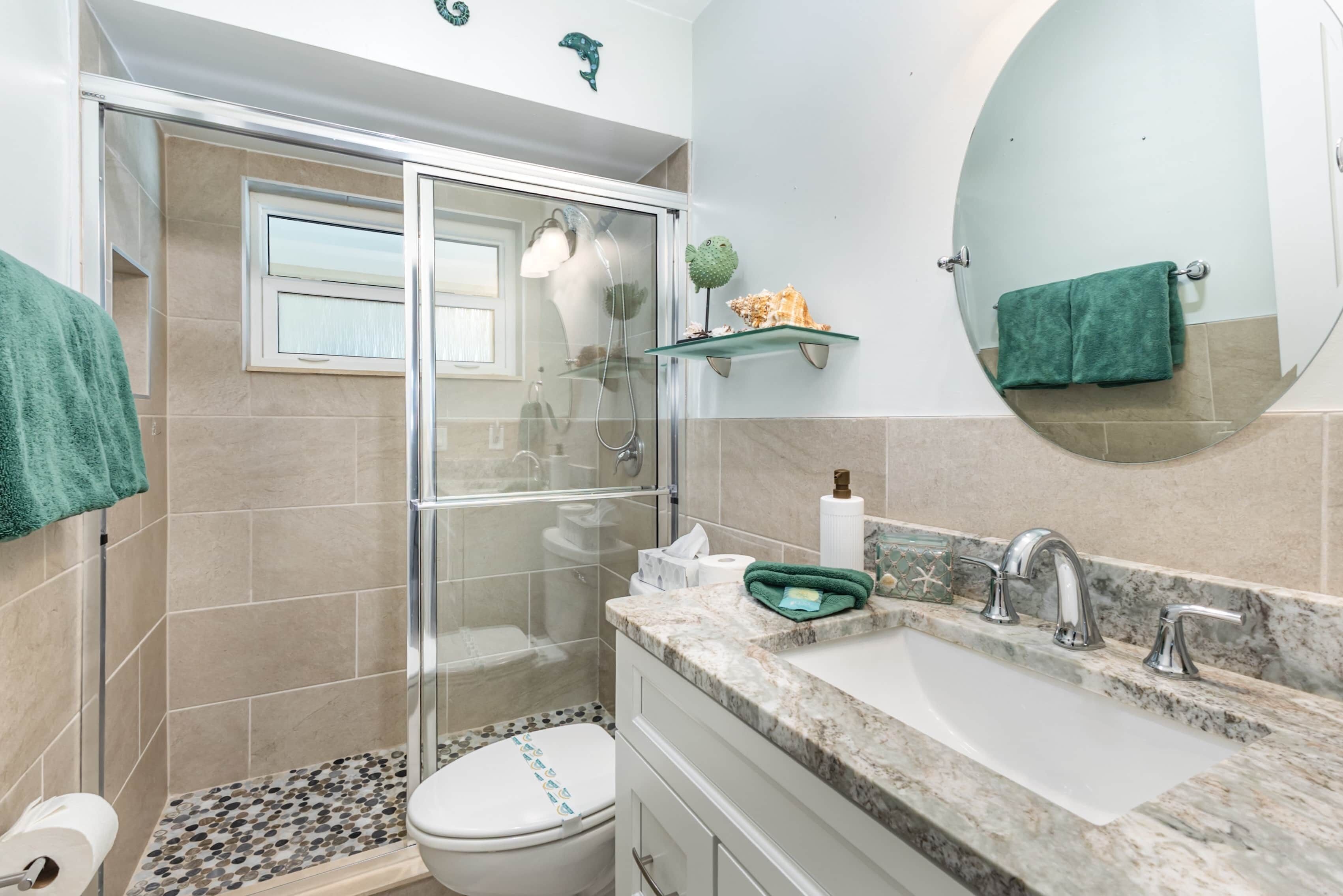 Un bagno con cabina doccia in vetro, un water, un lavabo con piano in marmo e uno specchio rotondo.