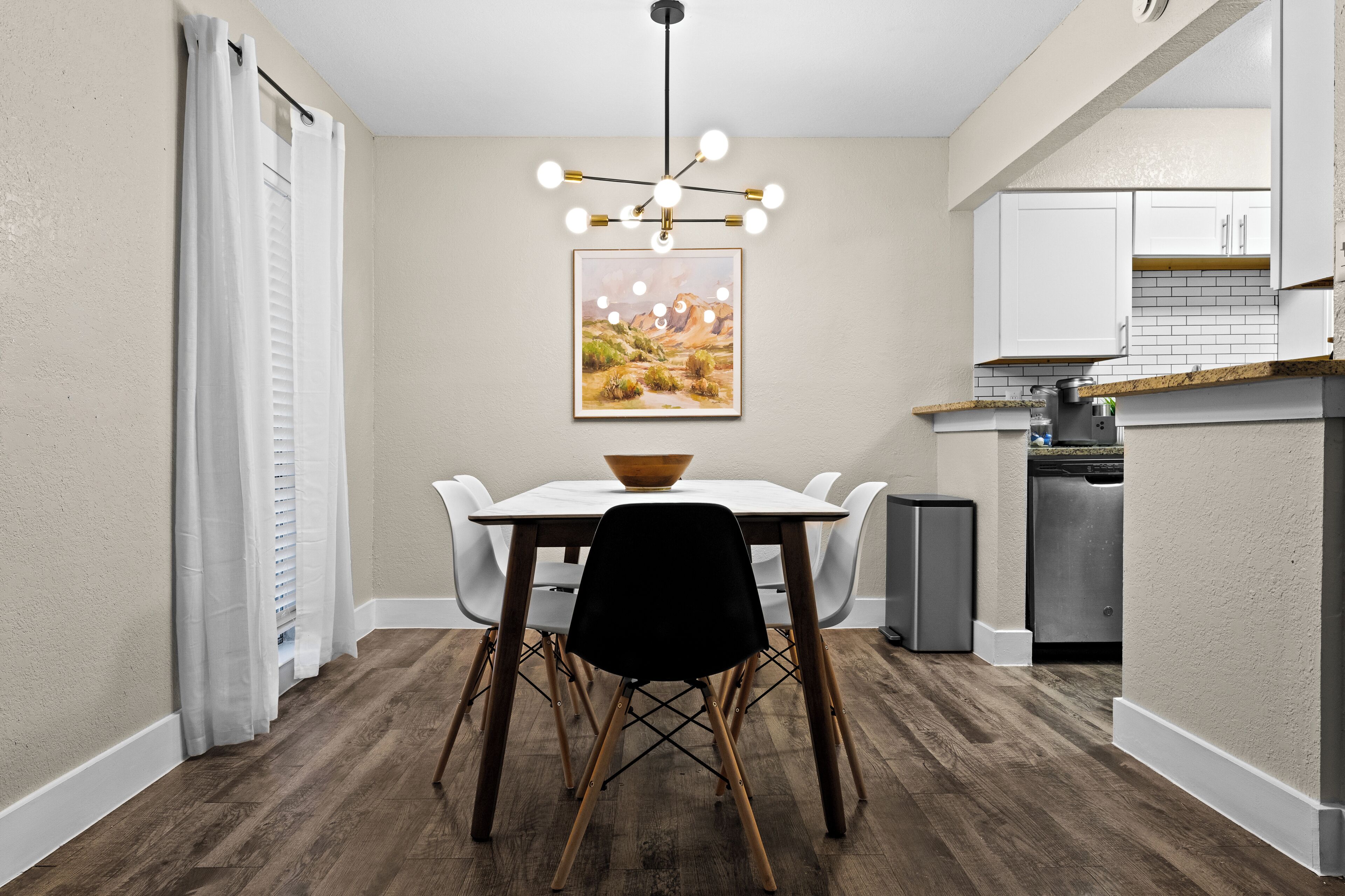 Un espace repas avec une table blanche, des chaises noires et un plancher en bois.