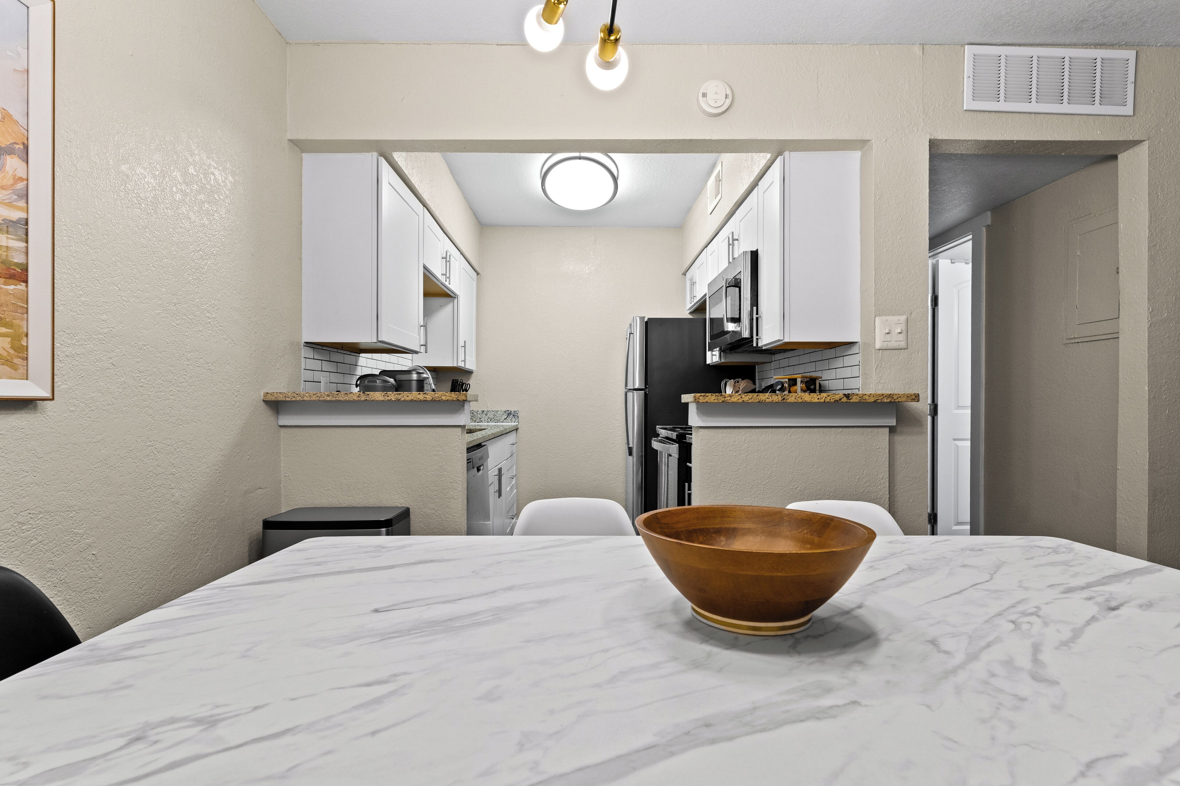 A modern kitchen with white cabinets, a marble countertop, and a wooden bowl on the table.