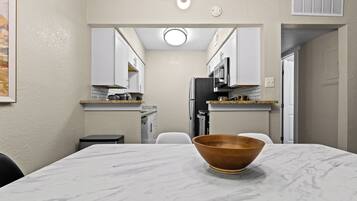 A modern kitchen with white cabinets, a marble countertop, and a wooden bowl on the table.