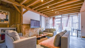 A cozy living room with a stone wall, wooden ceiling beams, a flat-screen TV, and a sliding glass door to the outside. - Le Gite du Relais - PARGUES (PARGUES)
