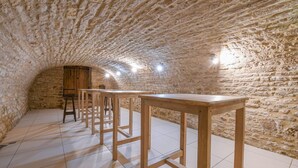 A stone-walled room with wooden tables and chairs, a wooden door, and a tiled floor. - Le Gite du Relais - PARGUES (PARGUES)