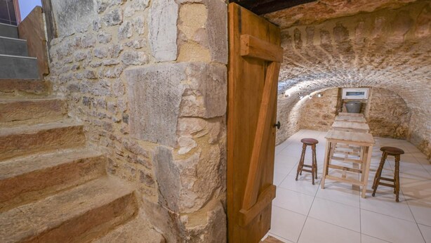 A stone-walled room with a wooden door, a staircase, and a small bar area with stools and a bar counter. - Le Gite du Relais - PARGUES (PARGUES)