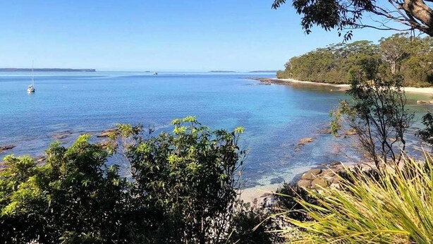 Eine Küstenlandschaft mit klarem, blauem Wasser, einem Sandstrand und dichter Vegetation.