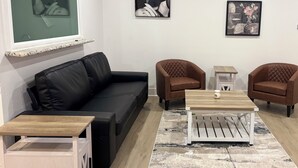Ein Wohnzimmer mit einer schwarzen Ledersofa, zwei braunen Sesseln, einem Holztisch und einem gemusterten Teppich.