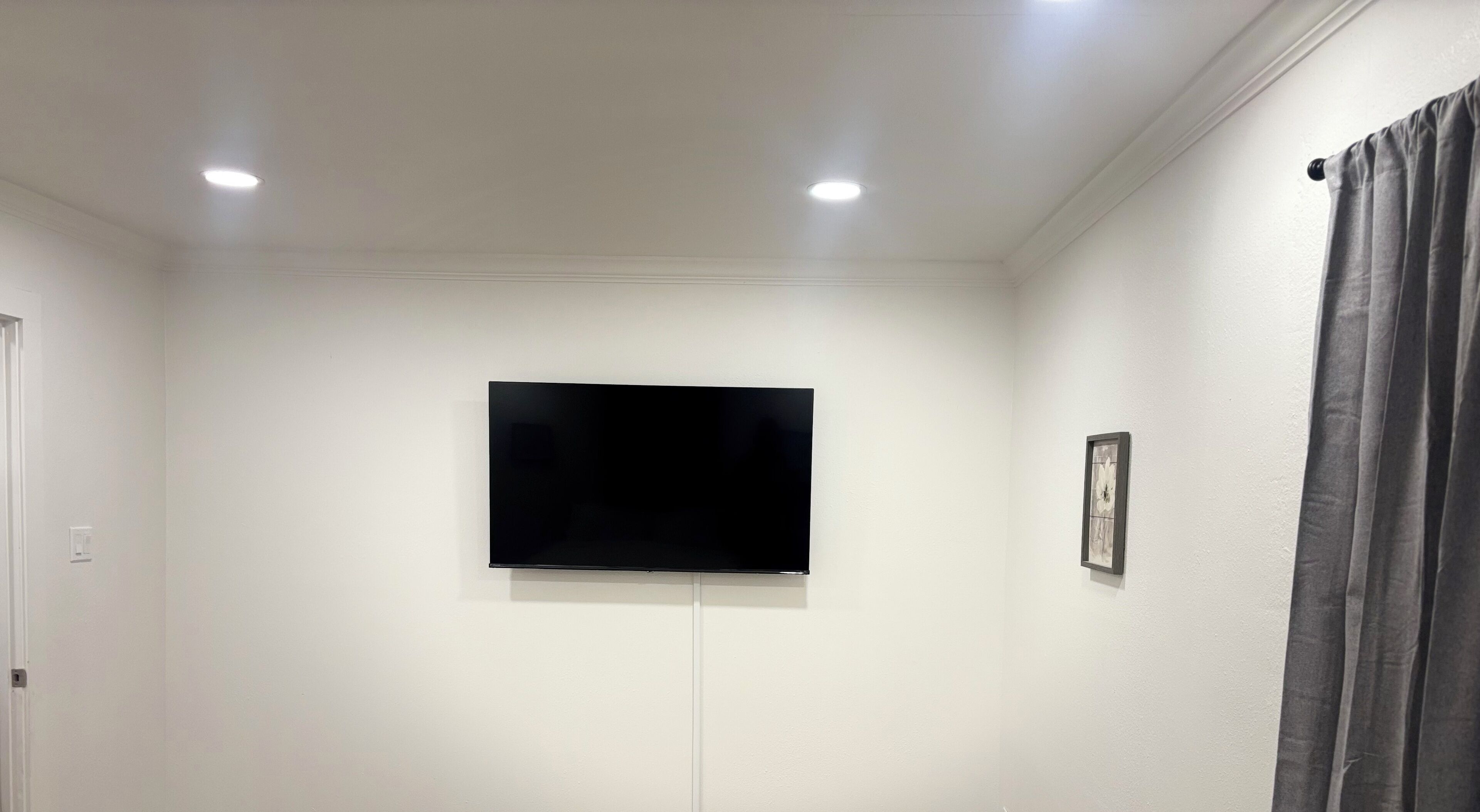 Et værelse med et fladskærms-tv monteret på væggen, en dør til venstre og en gardin til højre.