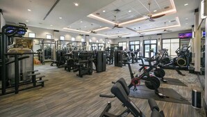 Une salle de sport équipée de divers appareils d’exercice, dotée d’un ventilateur de plafond et de grandes fenêtres.