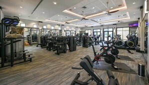 Une salle de sport équipée de divers appareils d’exercice, de ventilateurs au plafond et de grandes fenêtres.