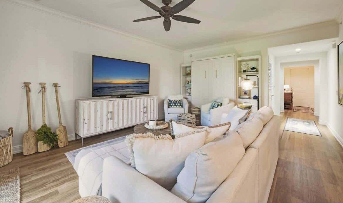 A living room with a sofa, a television, a ceiling fan, and a view of the ocean.