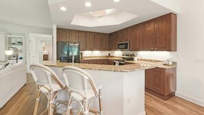 Une cuisine moderne avec des meubles en bois, un îlot central doté de tabourets de bar et des appareils électroménagers intégrés.