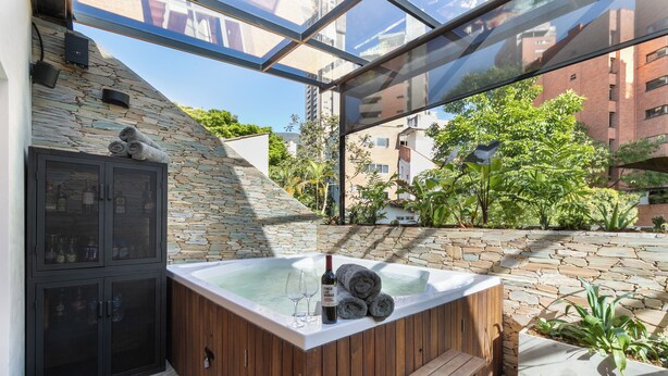 Jacuzzi amb un mur de pedra de fons, un banc de fusta i una zona de pati tancada amb vidre.