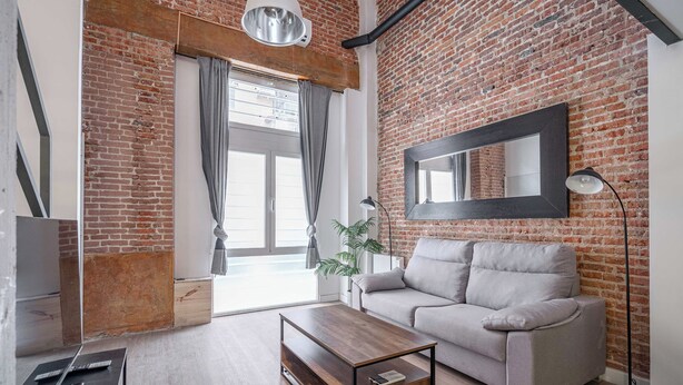 A modern living room with a brick wall, a grey sofa, a wooden coffee table, and a large mirror. - Deluxe Prosperidad Apartment (Madrid)