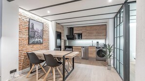 A modern kitchen with a brick wall, wooden cabinets, and a dining area with a table and chairs. - Deluxe Prosperidad Apartment (Madrid)