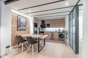 A modern kitchen with a brick wall, wooden cabinets, and a dining area with a table and chairs. - Deluxe Prosperidad Apartment (Madrid)