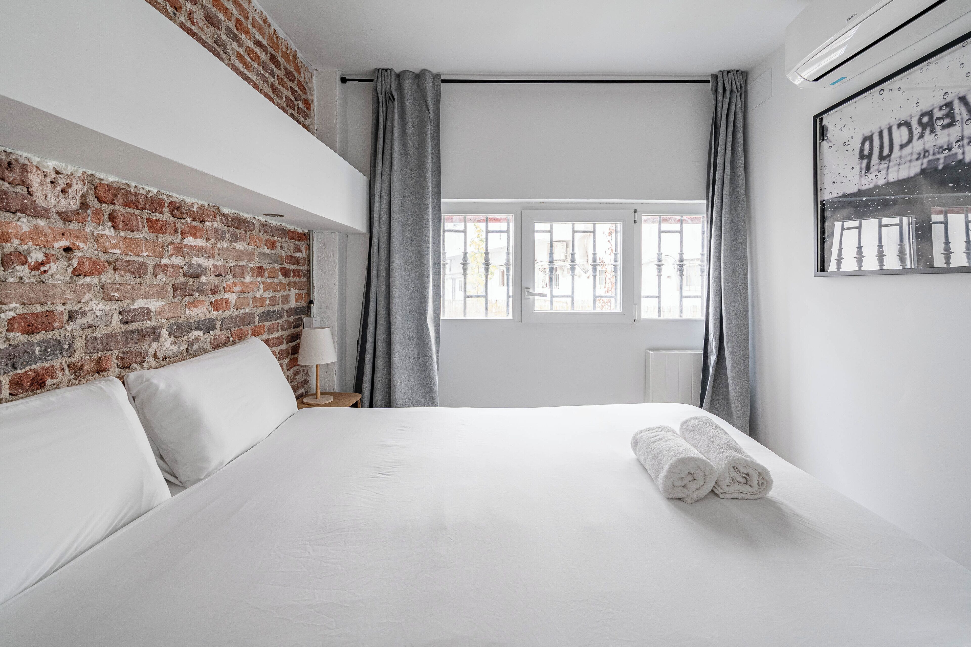Ein modernes Hotelzimmer mit einer Ziegelwand, einem ordentlich bezogenen Bett, einem Fenster mit Vorhängen und einer Heizung.