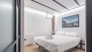 A modern bedroom with a large bed, a small bedside table, a wall-mounted radiator, and a window with a view of the sky. - Deluxe Prosperidad Apartment (Madrid)
