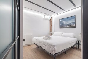 A modern bedroom with a large bed, a small bedside table, a wall-mounted radiator, and a window with a view of the sky. - Deluxe Prosperidad Apartment (Madrid)