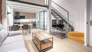 A modern living room with a sofa, coffee table, and a dining area with chairs. A staircase is visible in the background leading to an upper floor. - Deluxe Prosperidad Apartment (Madrid)