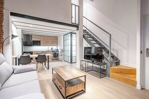A modern living room with a sofa, coffee table, and a dining area with chairs. A staircase is visible in the background leading to an upper floor. - Deluxe Prosperidad Apartment (Madrid)