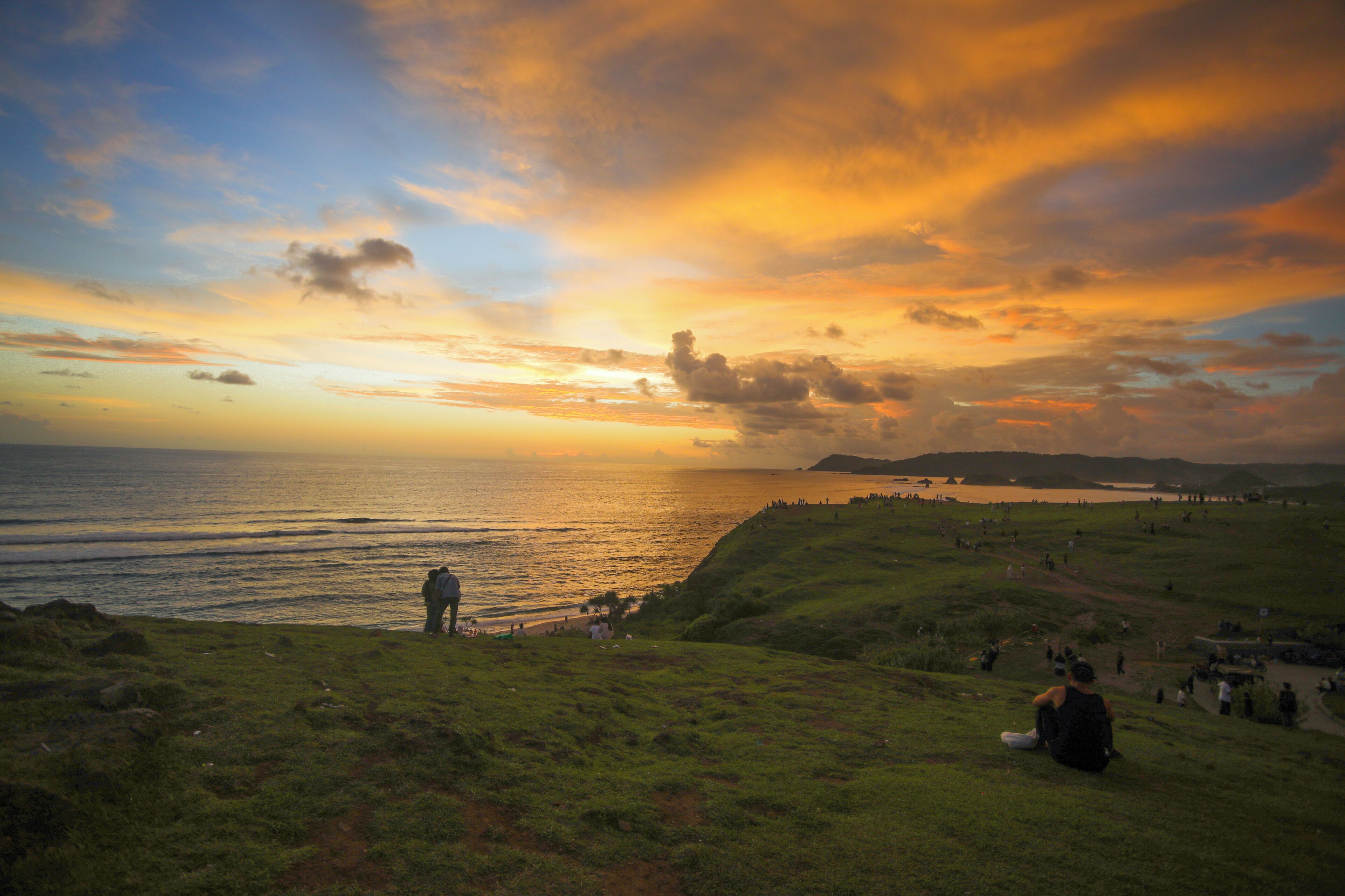 A coastal landscape with a sunset, grassy hills, and a view of the sea.