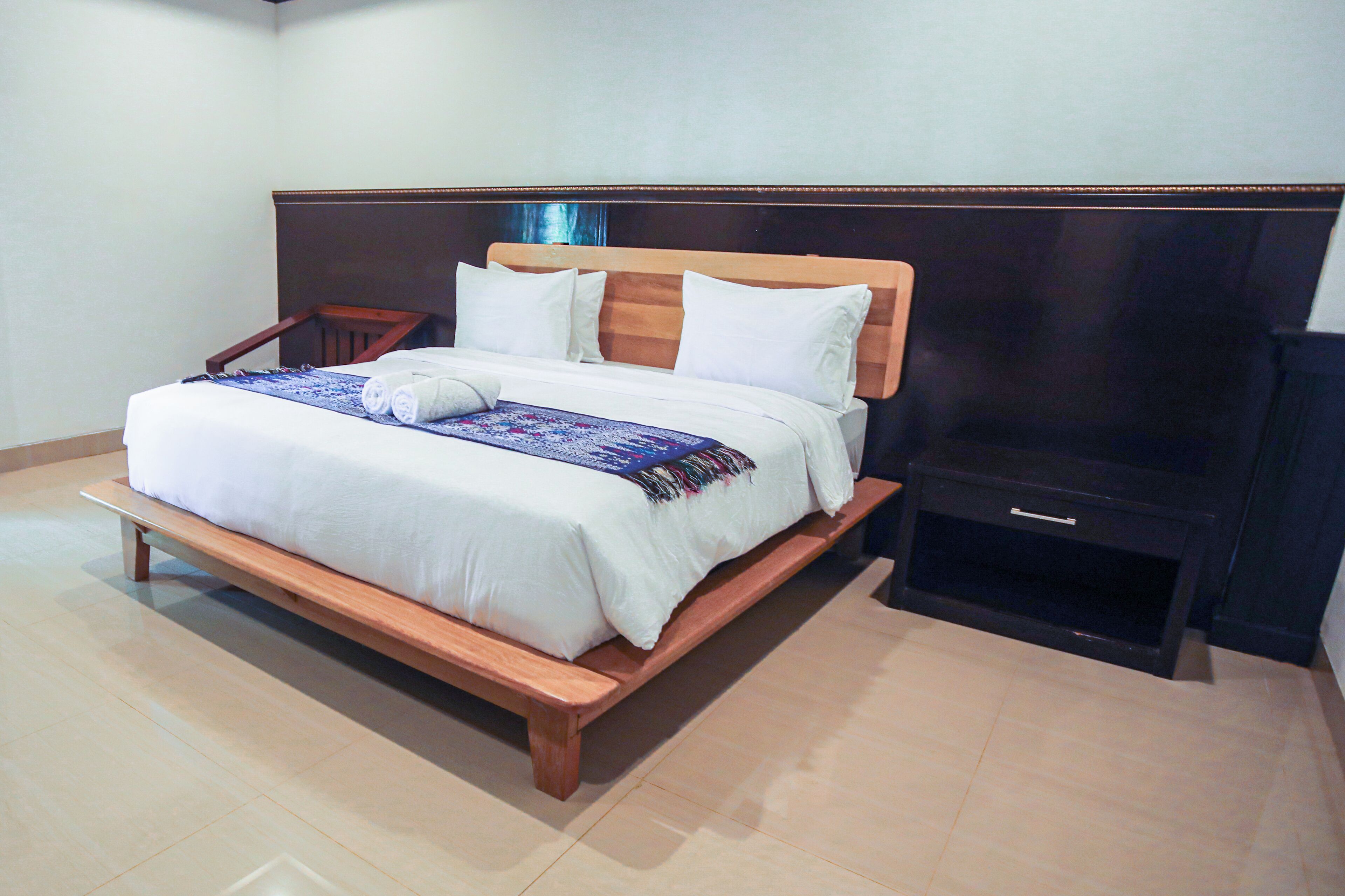 A neatly made bed with a wooden headboard, a bedside table, and a dark nightstand.