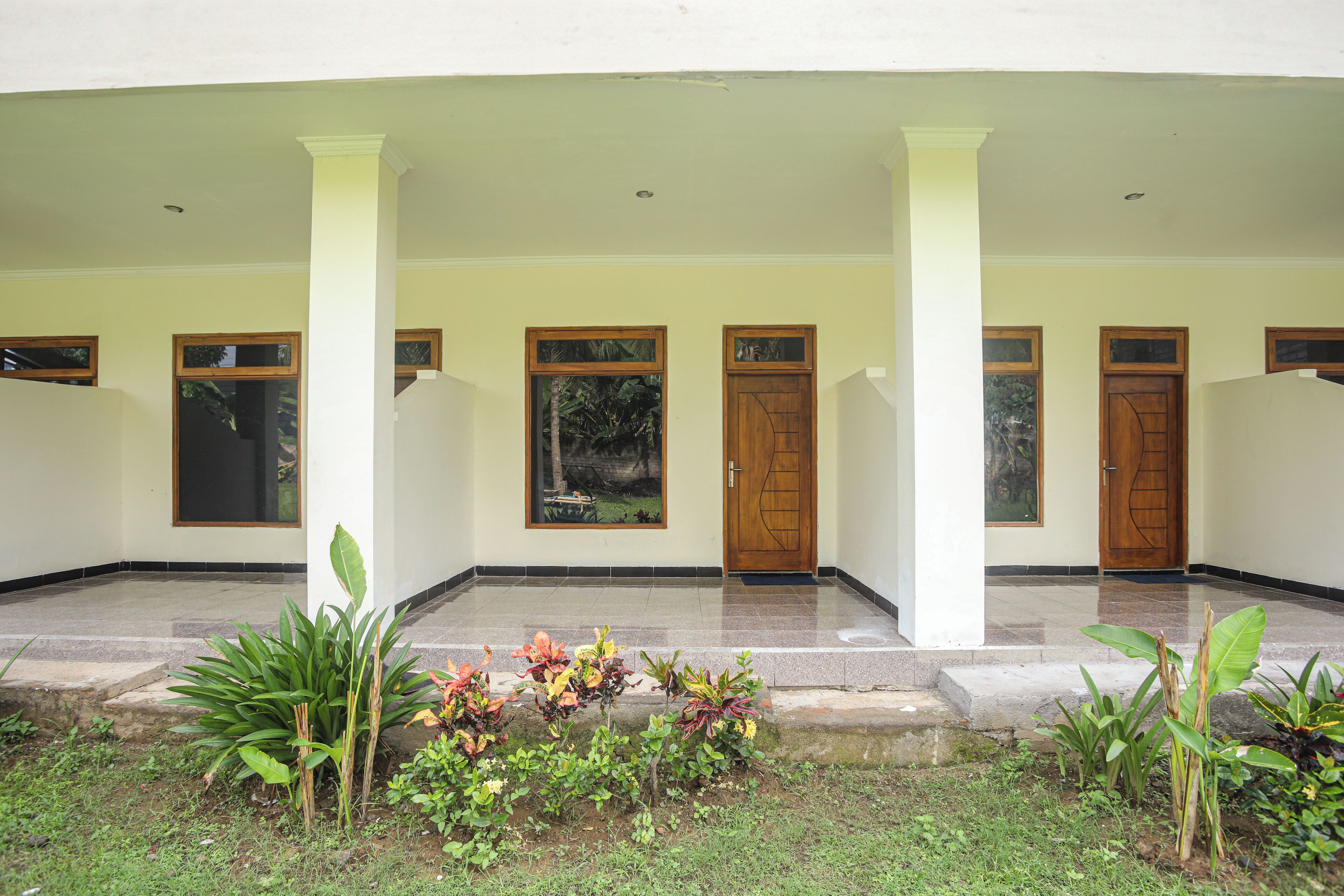 A covered entrance with a series of doors and windows, a tiled floor, and a small garden area with plants.