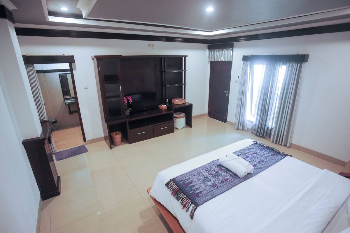 Un dormitorio con una cama grande, un armario, un televisor y una ventana con cortinas.