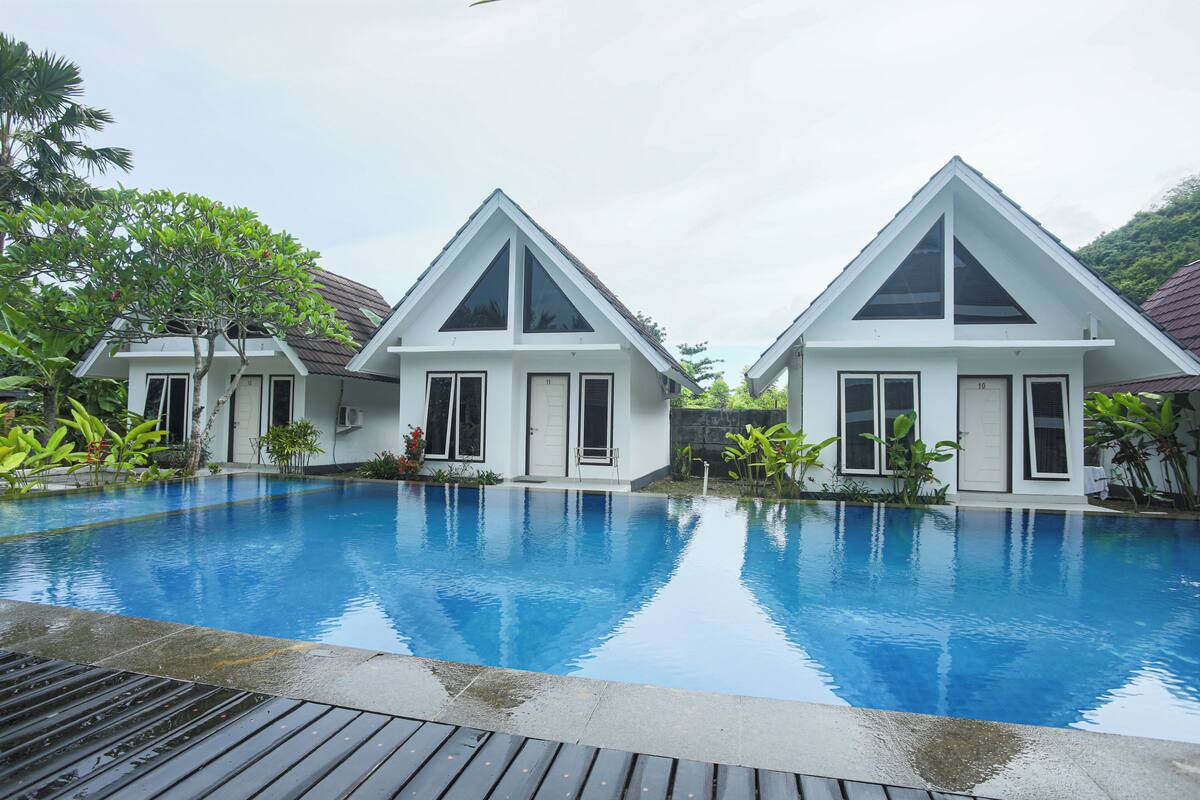 Un área de piscina moderna con dos edificios blancos, cada uno con techo triangular y ventanas amplias.