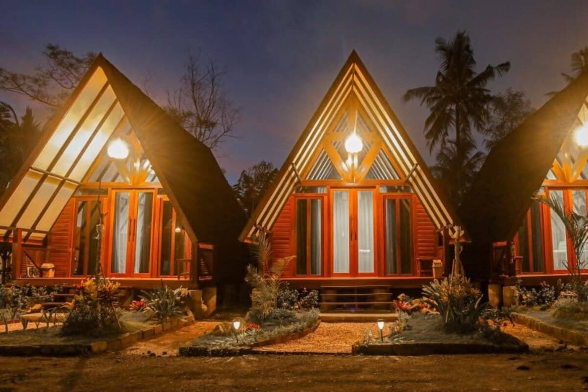 Tres cabañas de madera triangulares con ventanas grandes y una lámpara central.