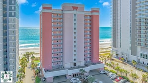 Un hotel de varios pisos con balcones, un estacionamiento y vistas a la playa y al océano.