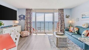 Una sala de estar con un sofá, una mesa, un televisor y un balcón con vistas.