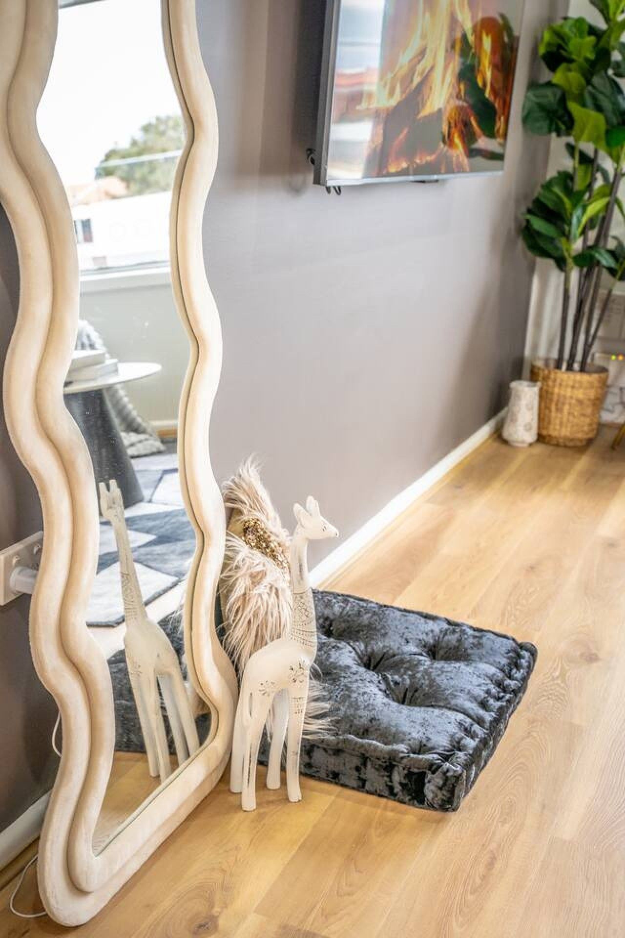 A room with a wavy mirror, a grey cushioned bench, and decorative animal figures.