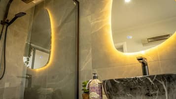 A bathroom with a glass-enclosed shower, a marble sink, and a wall-mounted mirror.