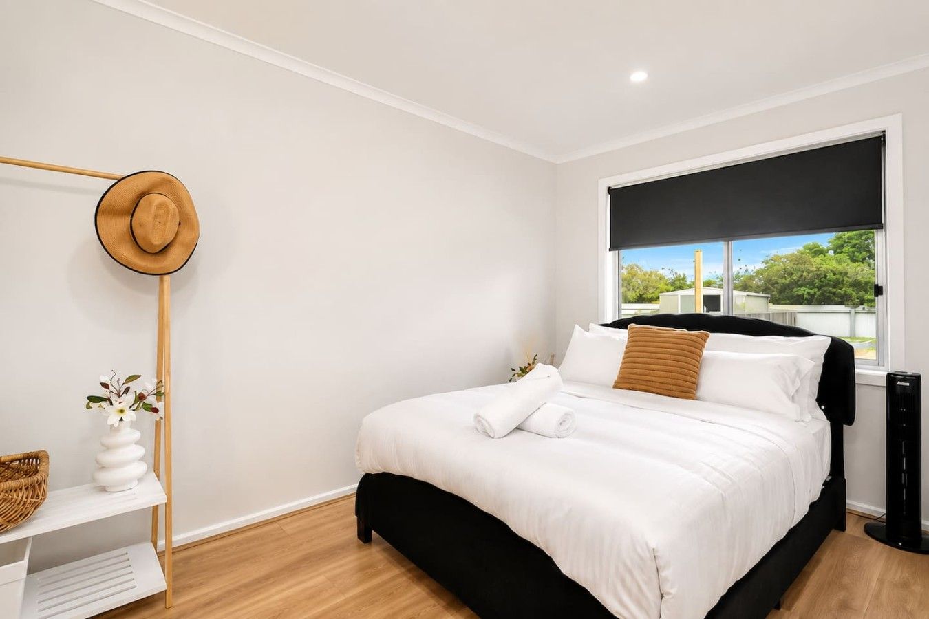 A modern bedroom with a bed, a window with a view, a hat on the wall, and a small table with a vase.