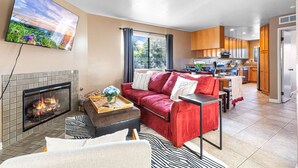 A modern living room with a fireplace, a red sofa, and a kitchen in the background. - Point Loma Hideaway · Relaxing Hot Tub + AC (San Diego)