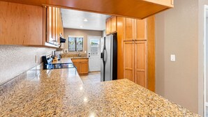 A kitchen with granite countertops, wooden cabinets, and a stainless steel refrigerator. - Point Loma Hideaway · Relaxing Hot Tub + AC (San Diego)