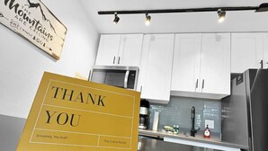 Eine moderne Küche mit weißen Schränken, Edelstahlgeräten und einem gelben Schild mit der Aufschrift 'THANK YOU' und einer Botschaft vom Personal.
