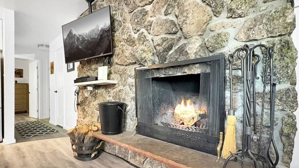 Ein Kamin aus Stein mit einem darüber montierten Fernseher, ein Holzkorb und ein Schürhaken.