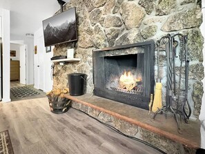 Ein Kamin aus Stein mit einem darüber montierten Fernseher, ein Holzkorb und ein Schürhaken.
