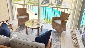 En balkon med fletstole, et lille bord og en sofa. En pool er synlig i baggrunden.