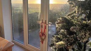 Une pièce dotée d’une grande fenêtre donnant sur un paysage enneigé et ornée d’un sapin de Noël décoré.