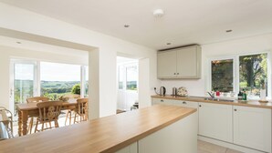 Une cuisine moderne avec un plan de travail en bois, des armoires blanches et une vue sur la campagne grâce à de grandes fenêtres.