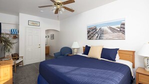 Ein Schlafzimmer mit einem großen Bett, einem Deckenventilator, einem Gemälde eines Piers und einer Tür, die in einen anderen Raum führt.