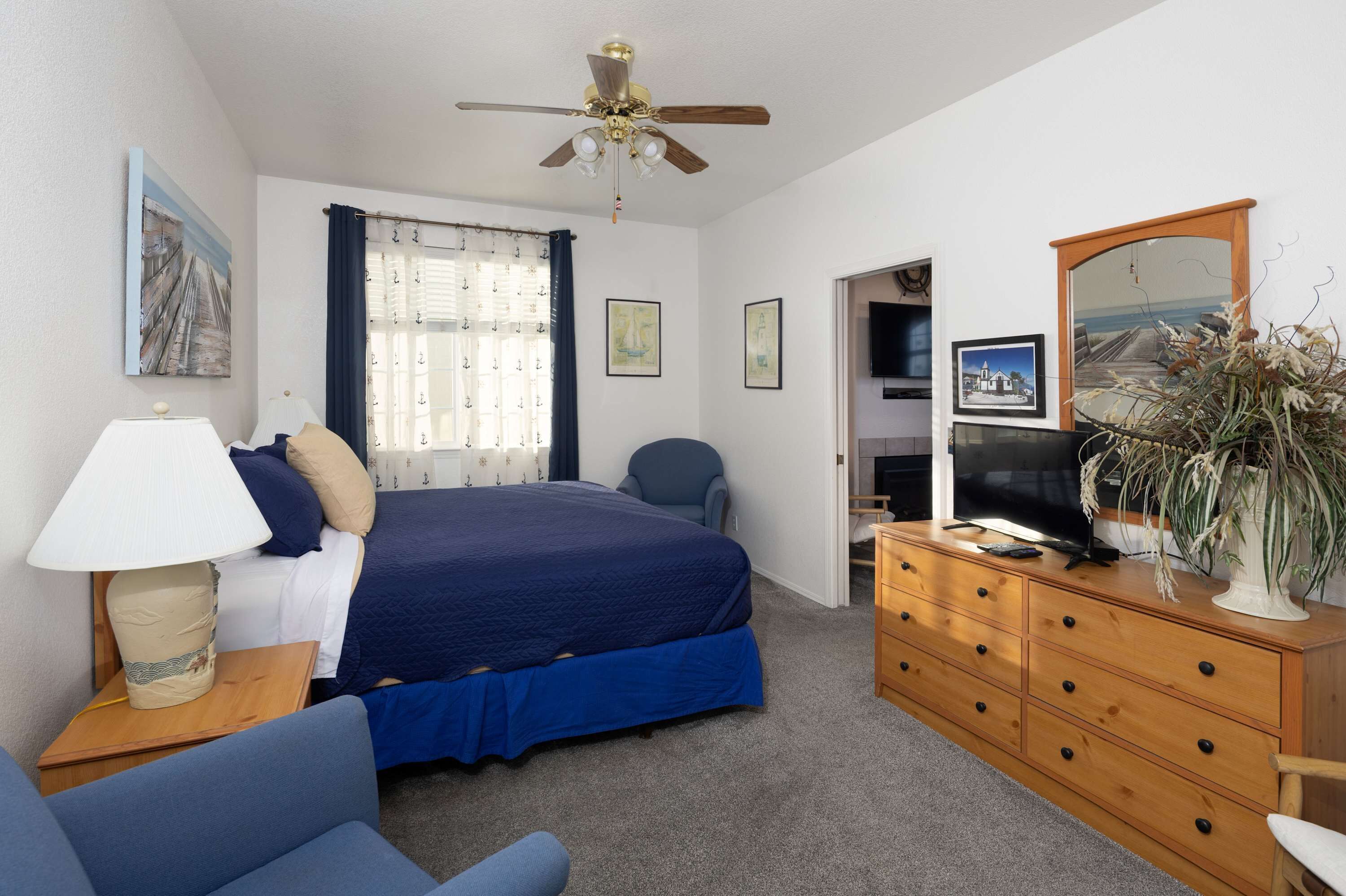 Un dormitorio con cama, escritorio, silla, cómoda, televisor y ventilador de techo.