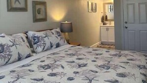 Un dormitorio con cama, ventilador de techo, decoración de estrellas de mar en la pared y una puerta que da a un baño.
