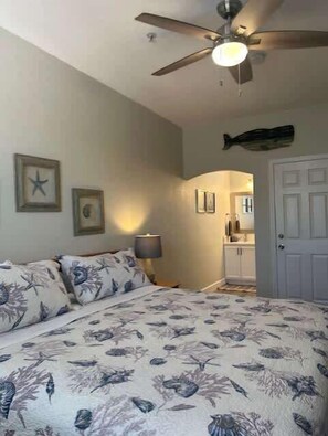 A bedroom with a bed, ceiling fan, wall-mounted starfish decorations, and a door leading to a bathroom. - The Tranquil Terrace (Oceano)